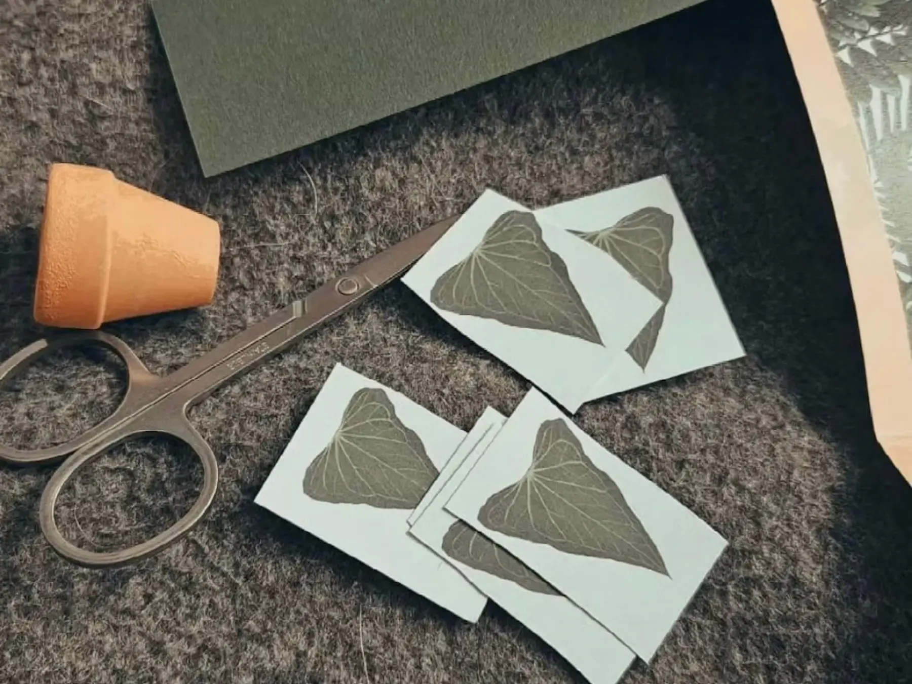 Paper leaves, scissors, and a tiny terracotta pot on felt