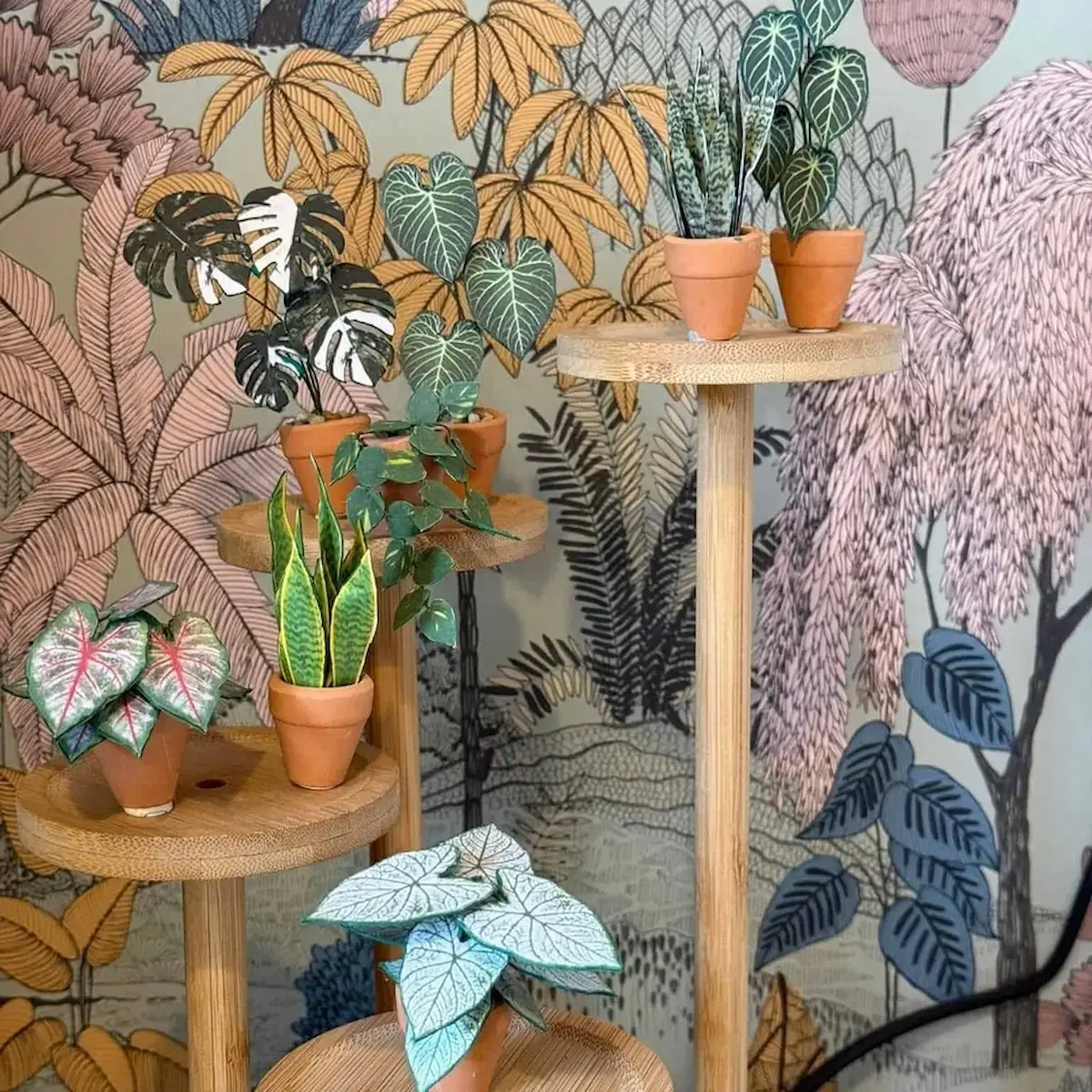 Miniature paper plants on round wooden pedestals with botanical wallpaper
